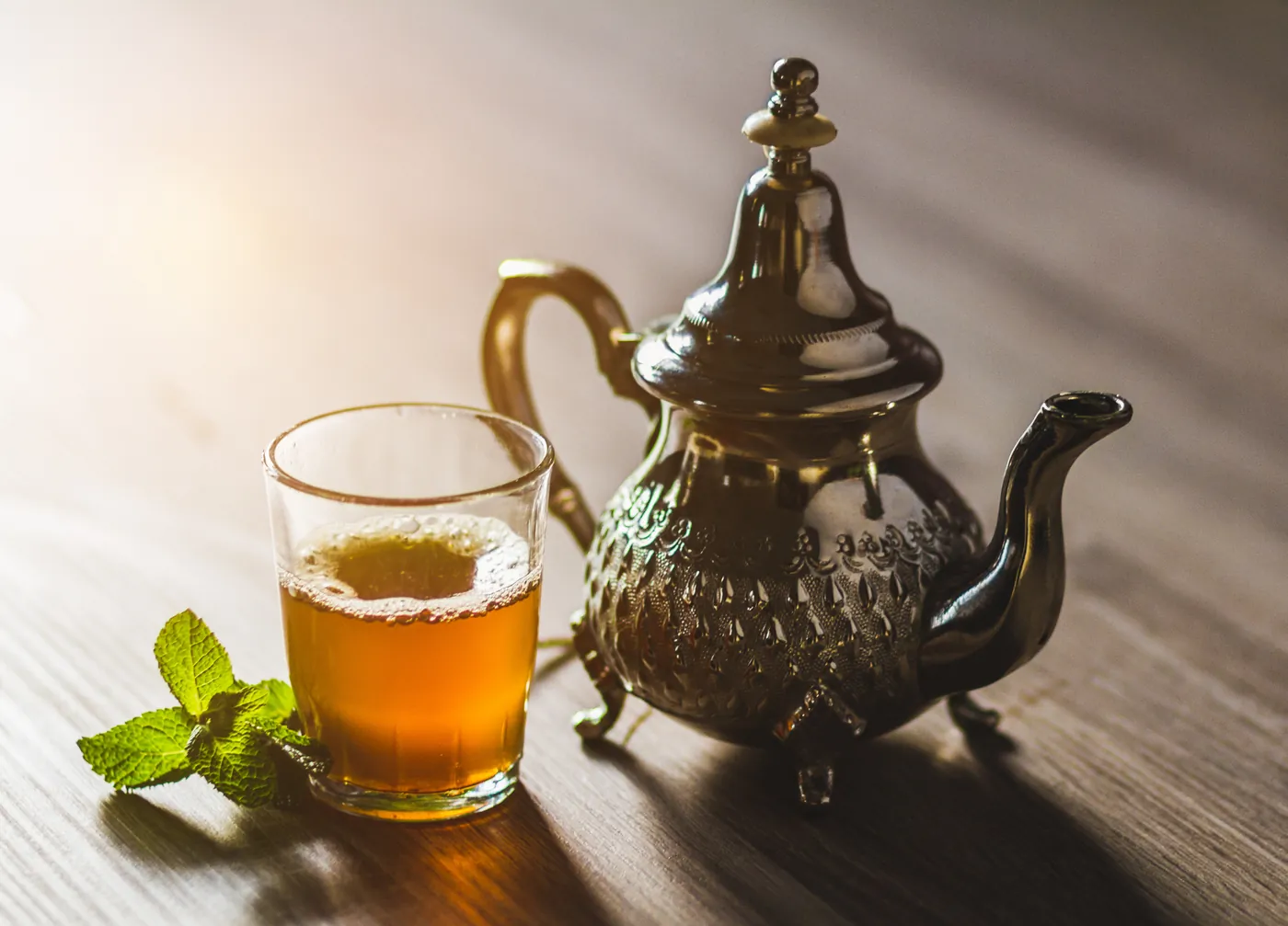Verre de thé à la menthe devant une théière marocaine