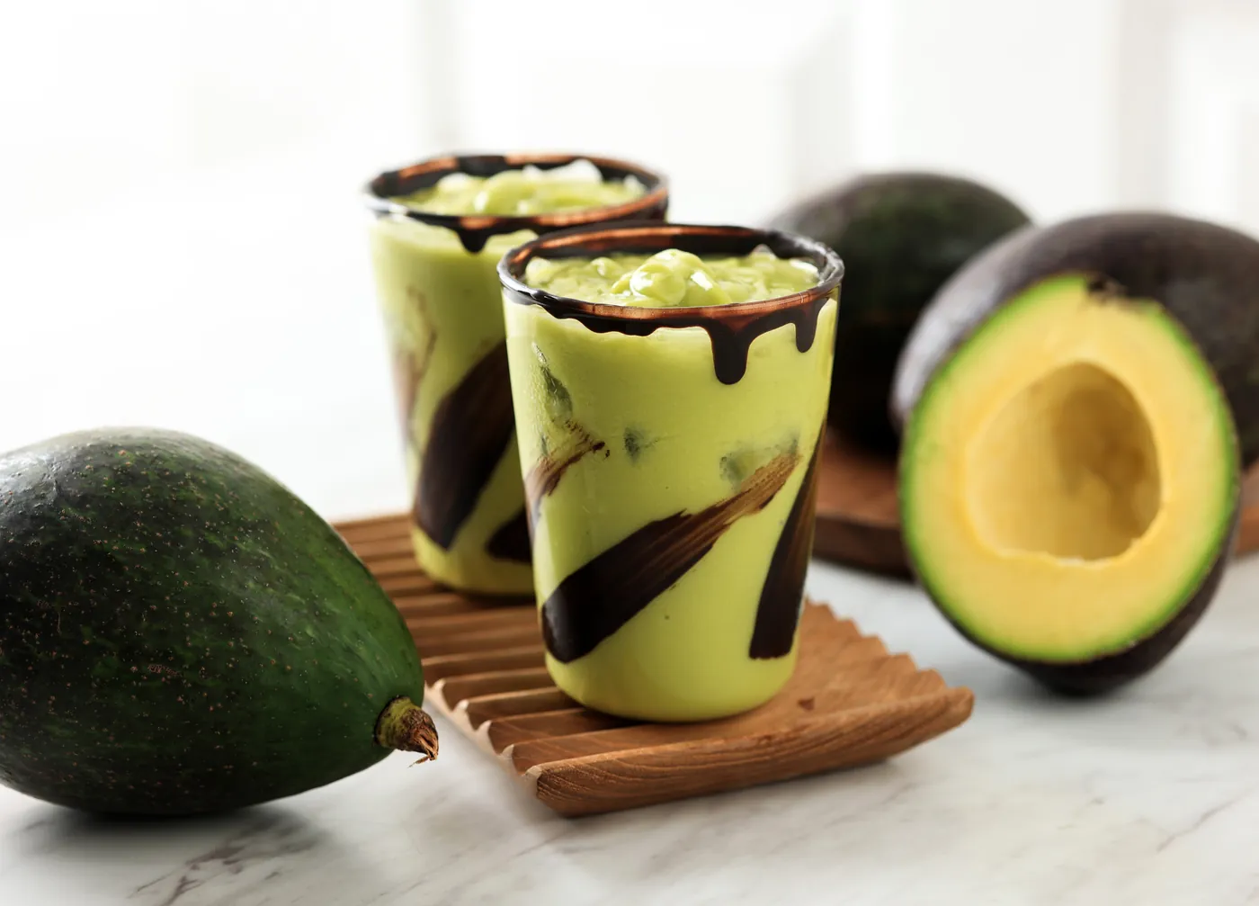 Deux verres de jus d’avocat nappés de chocolat, avocats autour